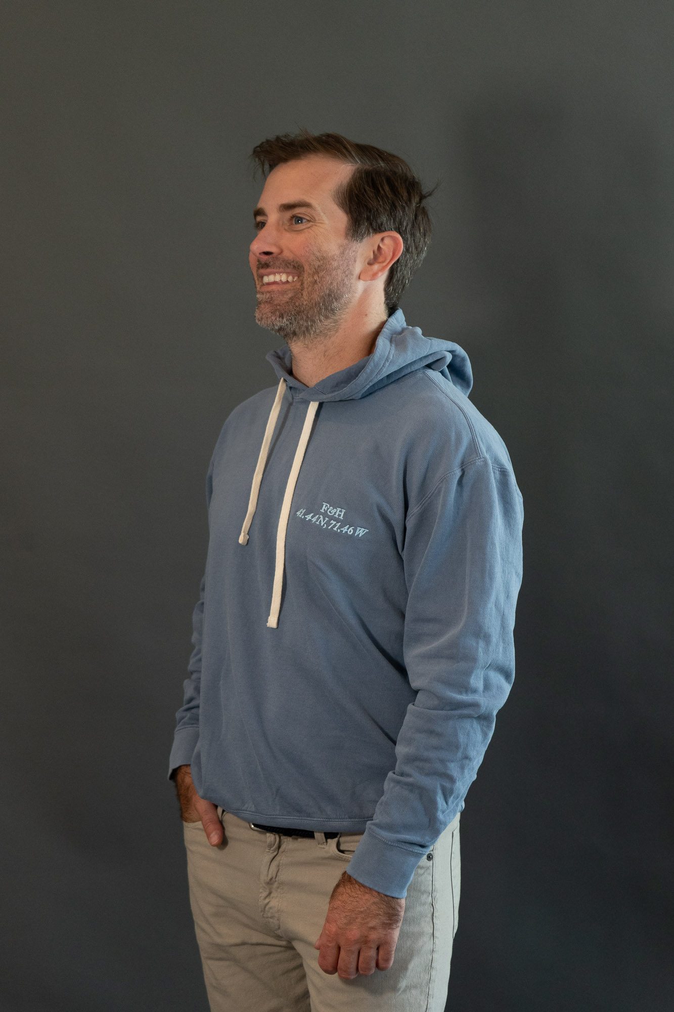 The Narragansett Saltwash Hoodie in blue jean, worn, with the F&H monogram and the coordinates 41.44 N, 71.46 W stitched at the chest