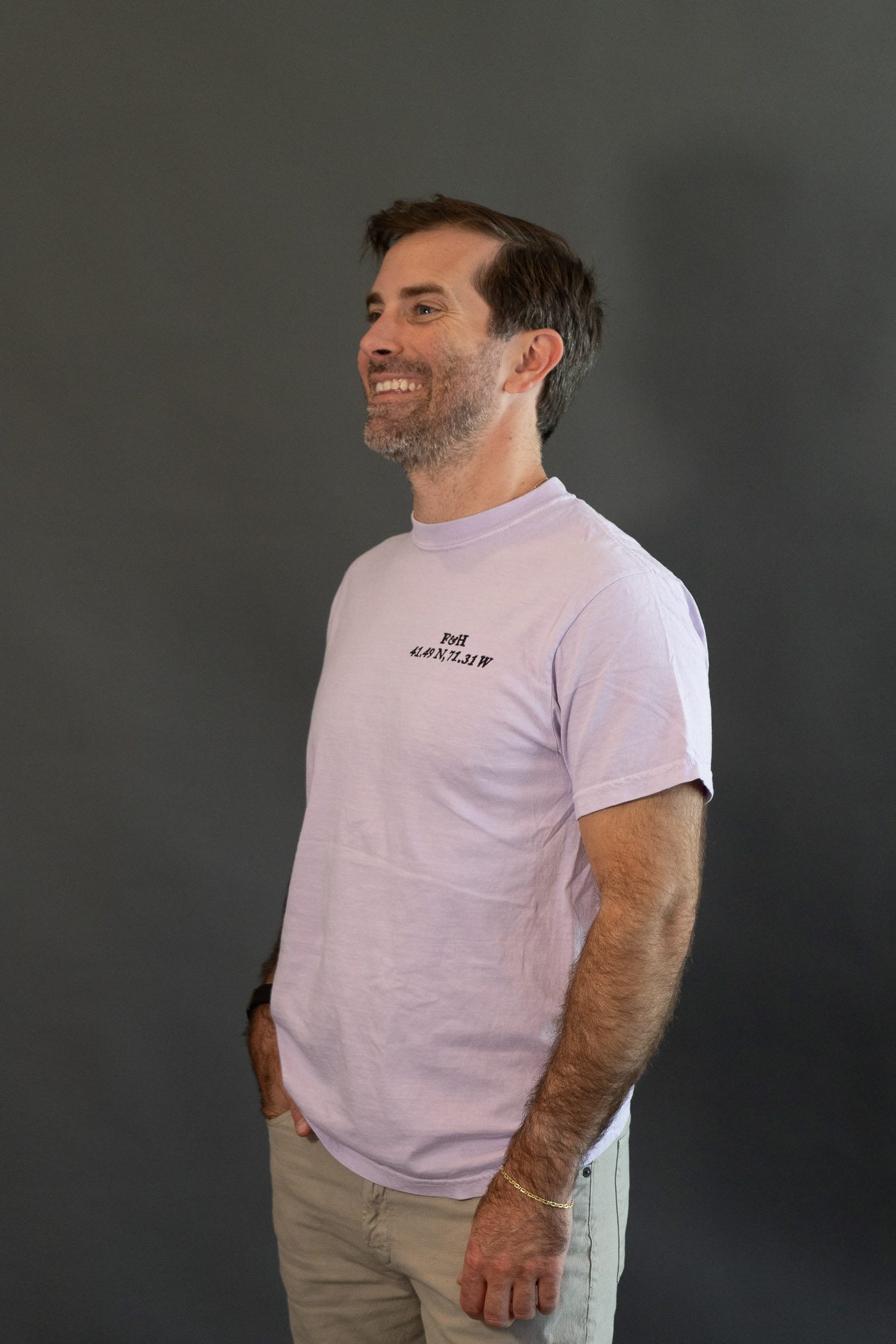 The Newport Saltwash Tee in orchid, worn, with the F&H monogram and the coordinates 41.49 N, 71.31 W stitched at the chest