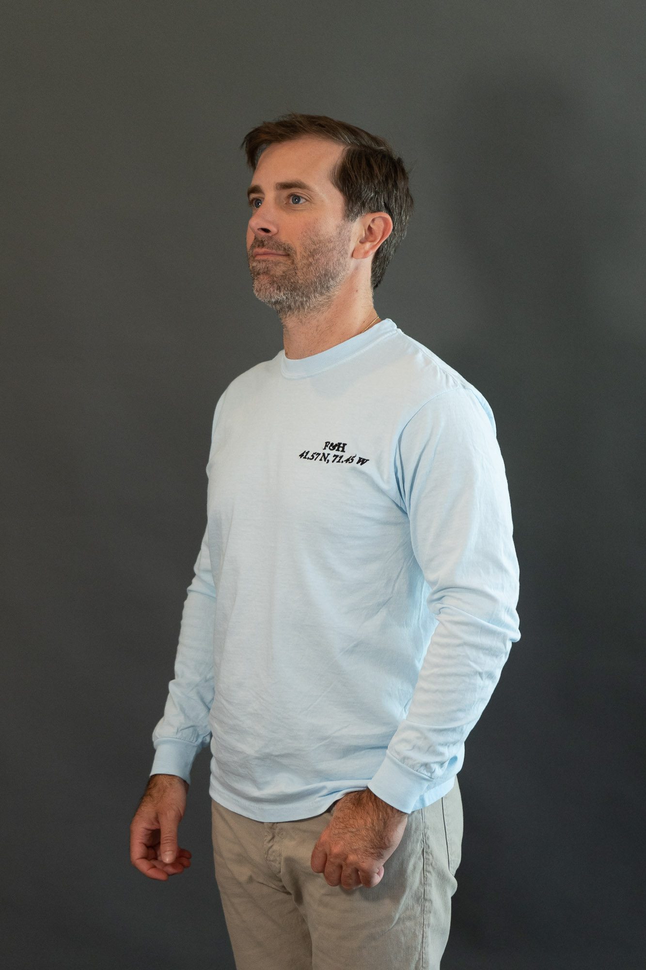 The Wickford Saltwash Long Sleeve Tee in chambray, worn, with the F&H monogram and the coordinates 41.57 N, 71.45 W stitched at the chest
